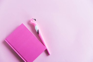 Notlar için pembe defter, pembe pastel arka planda komik flamingo kalem. Düz yatıyordu. Üst Manzara. Boşluğu kopyala