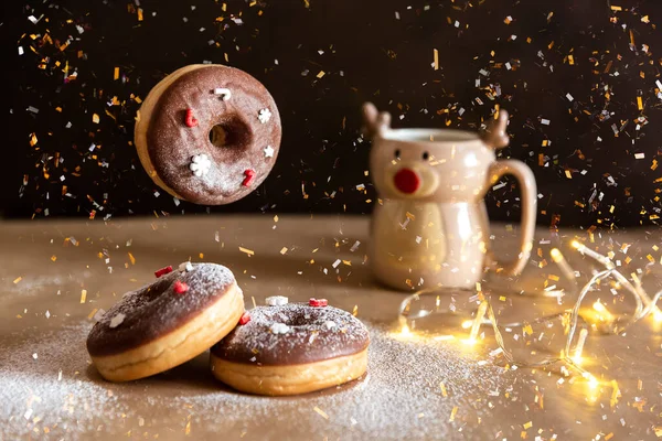 Christmas breakfast table with flying chocolate donut decorated with red and white sprinkles, hot cocoa in deer mug on background — Stock Photo, Image