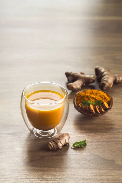 Organic orange turmeric drink, tea with cinnamon in a glass mug with fresh turmeric powder on wooden background. Indian oriental low cholesterol spices. Food and drink, diet nutrition