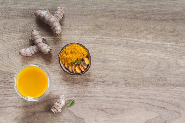 Organic orange turmeric drink, tea with cinnamon in a glass mug with fresh turmeric powder on wooden background. Food and drink, diet nutrition, health care concept. Top view. Copy space.