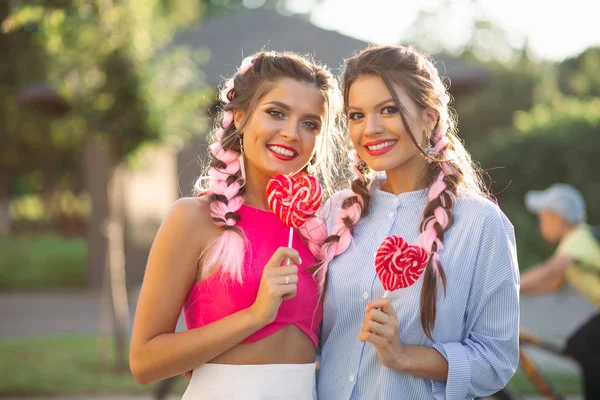 Девушки с разноцветными косичками, держащие конфетное сердце на палочке . — стоковое фото