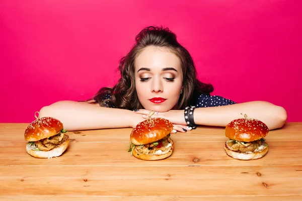 Chica triste mirando deliciosas hamburguesas frescas con pollo en t de madera —  Fotos de Stock