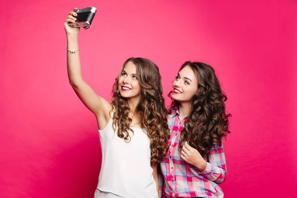 Studio Portrait of happy nice girls in retro style with long wavy hair. Giving selfie to an old film camera. The brunette in a checkered shirt makes an emphasis on the hair holding them by hand. — Stock Photo, Image