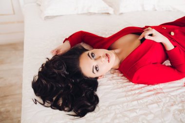 Kırmızı elbiseli seksi kız, gözleri kapalı yatağa uzanıyor..
