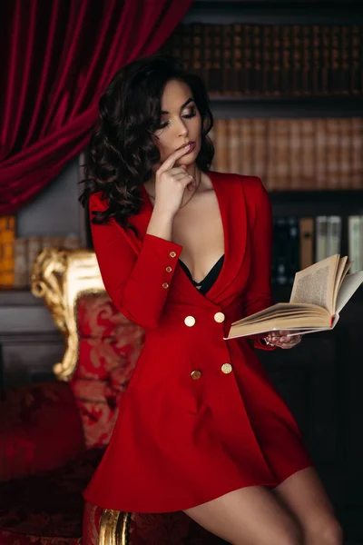Elegante bruna in rosso seduta su e con un libro in mano . — Foto Stock