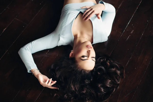上のビューの美しい女性で青いドレス暗い木製の床に横たわって. — ストック写真