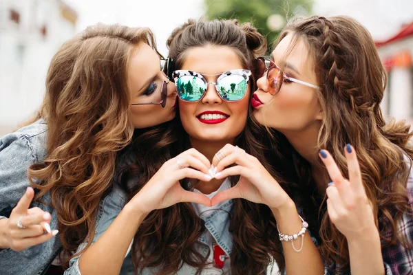 Gorgeous teenagers in sunglasses kissing their friend smiling at camera with heart gesture. — Stock Photo, Image