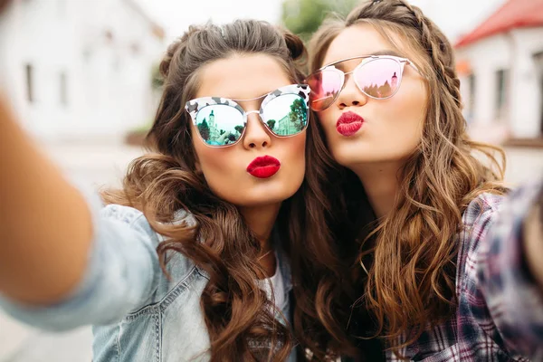 Hinreißende brünette Freundinnen mit Frisur, verspiegelter Sonnenbrille und roten Lippen machen Selfie mit Entengesicht. — Stockfoto