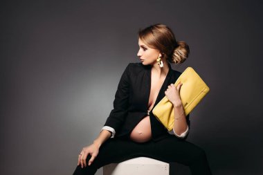 Siyah stüdyo arka planı oturan zarif hamile kadın.