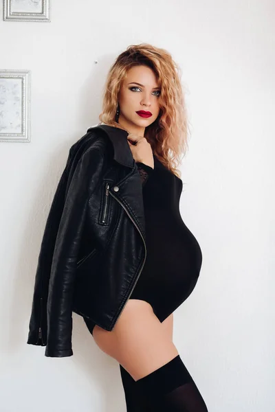 Módní sexy žena čeká dítě v černé těleso a koženou bundu. — Stock fotografie