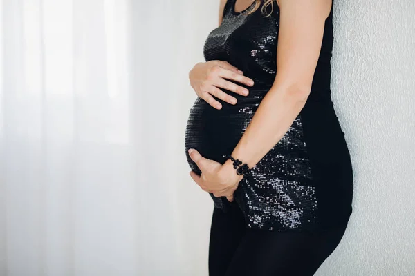 Mulher grávida em preto espumante top abraçando barriga sobre fundo branco . — Fotografia de Stock