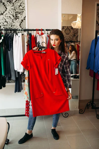 Swag y hermosa mujer sosteniendo y mostrando en la cámara vestido rojo . — Foto de Stock