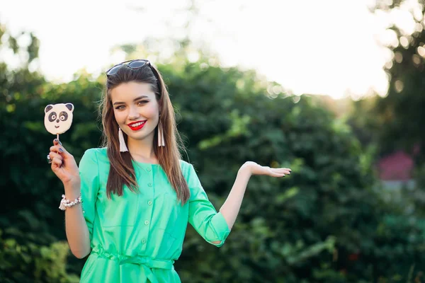 Lächelndes schönes Mädchen in grün, das sich an der Seite zeigt und Süßigkeiten hält wie ein Panda. — Stockfoto