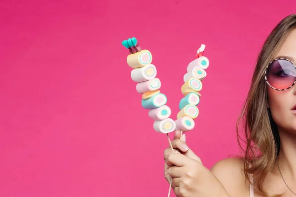 Seductive girl in pink sunglasses posing with marshmallow candy.