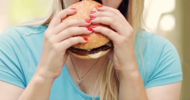 Mulher comendo hambúrguer, segurando por duas mãos . — Vídeo de Stock