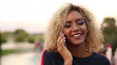 Işıklı kıvırcık saçlı konuşmak çağrı telefon ve gülümseyen pozitif kadın.