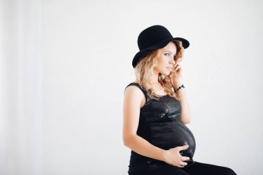 Siyah şapka ve köpüklü üst karnı kucaklayan şık hamile kadın.