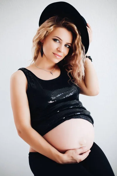 黒い帽子と彼女の腹を受け入れ輝くトップでスタイリッシュな妊娠中の女性. — ストック写真