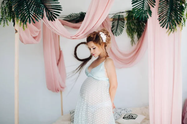 Bella donna incinta in abito da notte posa all'interno decorazione con fiori . — Foto Stock
