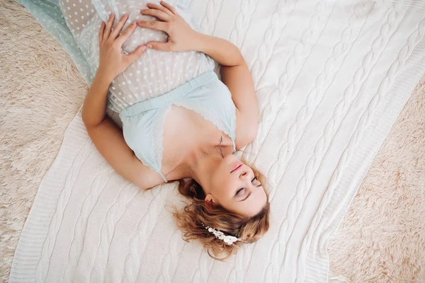 Blonde pregnant woman lying on bedtouching by hands on stomach. — Stock Photo, Image