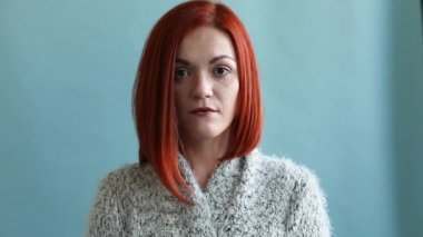 Uzun bir hırka Kızıl saçlı bir kadın çok şok. Kız gözleri geniş açılır ve sürpriz ağzını açar, sonra onu elleriyle kapsar. Yakın çekim. Mavi bir arka plan üzerinde izole. Stüdyo stok