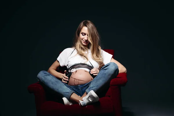 Mujer embarazada sentada en silla de lectura, mostrando barriga y posando . —  Fotos de Stock