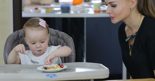 Linda niñita sentada en una silla para niños y compartiendo comida con su mamá . — Vídeos de Stock