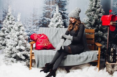 Gri Noel ağacı arasında bankta oturan kadın.