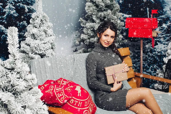 Atractiva mujer en vestido de punto con regalo de Navidad en el banco c —  Fotos de Stock
