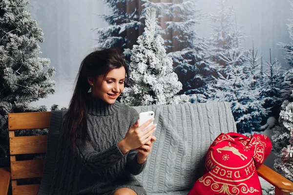 Leende glad tjej i stickad klänning med mobiltelefon över jult — Stockfoto