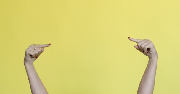 Weibliche Hände gestikulieren auf etwas auf gelbem Hintergrund. — Stockvideo