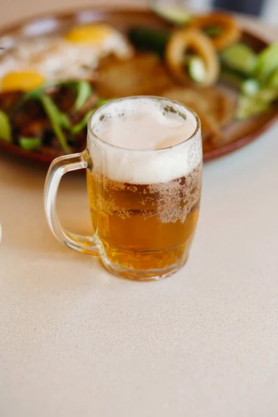 Vertical shot of cold beer cup standing near appetizers plate.