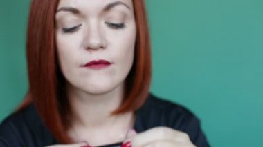 Kameraya bakarak ve tarafından kırmızı ruj dudakları çizim güzel ve kendinden emin kırmızı saçlı kadın odaklanmak. Studio yeşil zemin üzerine çok kadın poz ve kendisi için makyaj yapıyor.