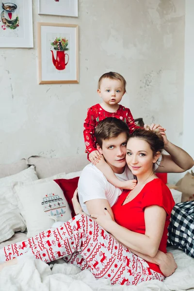 Retrato de familia en pijama sentados juntos en cama en dormitorio decorado para Navidad y abrazando . —  Fotos de Stock