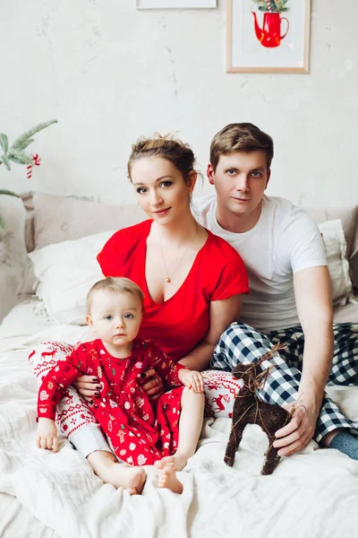 Retrato de família de pijama sentados juntos na cama no quarto decorado para o Natal e abraçando . — Fotografia de Stock