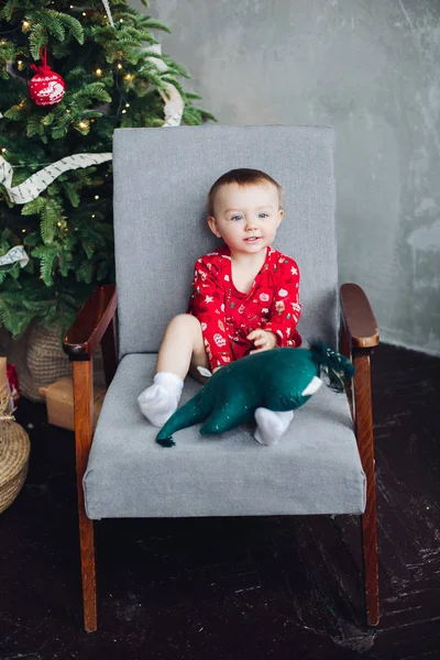 Adorable niño en vestido rojo con estampado de Navidad sentado en silla . — Foto de Stock