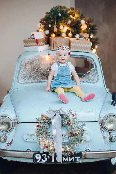 Vista frontal de la niña linda dulce y de moda sentado en el coche retro azul decorado para Navidad . — Foto de Stock