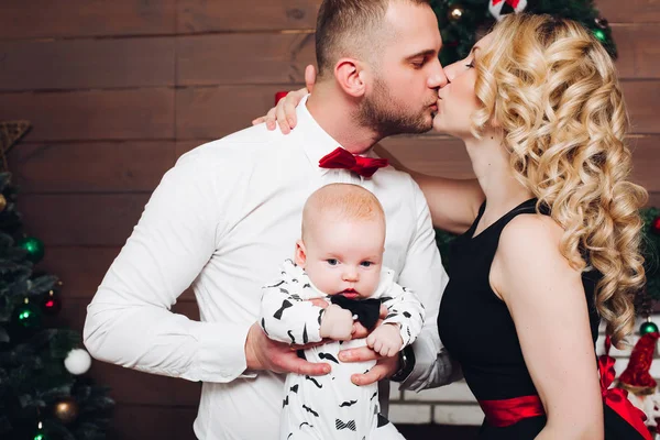 Elegancia de la familia de pie junto a la chimenea, abrazando a su hijo y besándose . —  Fotos de Stock