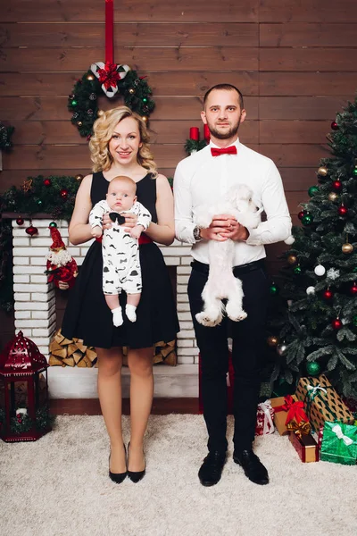 Funny family standing near fireplace holding dog and son in hands and smiling. — Stock Photo, Image