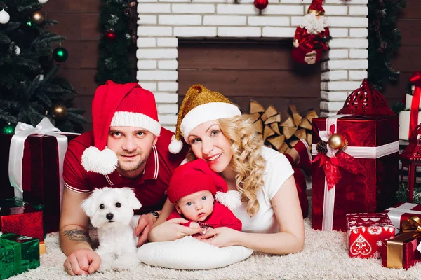 Familie op vloer liggen in de buurt van open haard met kleine zoon en hond en lachend op camera. — Stockfoto