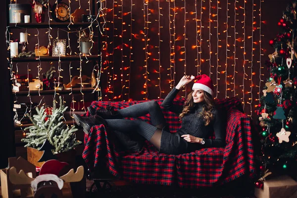 Mulher bonita vestindo em santa chapéu descansando no sofá . — Fotografia de Stock