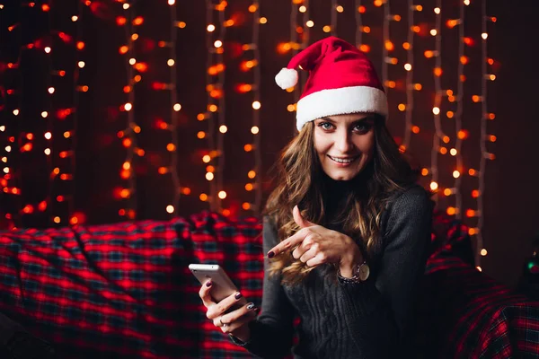 스마트 폰에서 손가락으로 가리키는 산타 모자에 있는 여자. — 스톡 사진