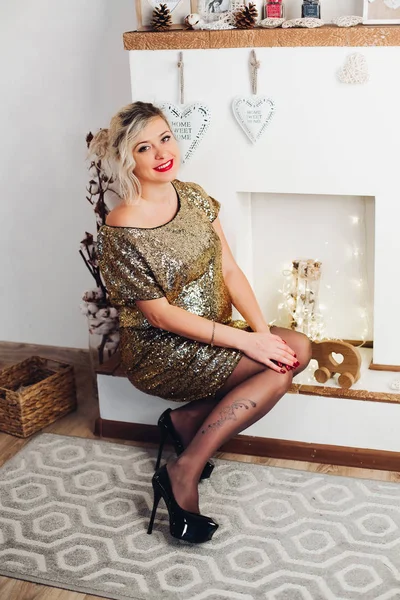 Красива усміхнена жінка в яскраво-золотій сукні, що сидить біля каміна . — стокове фото