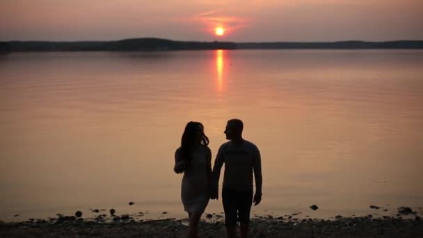 Sziluettjét a romantikus pár, séta a tó partján, és megcsókolta a naplemente. — Stock videók
