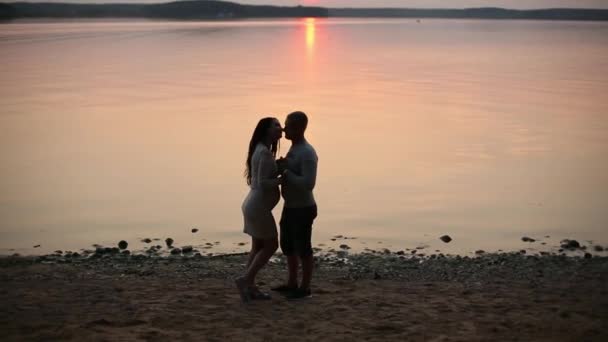 Sziluettjét a romantikus pár, séta a tó partján, és megcsókolta a naplemente. — Stock videók