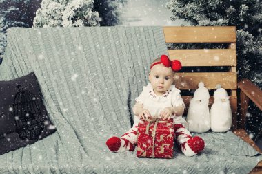 Bebek güzel kız şirin elbise ile lots-in Noel bankta oturmuş kafa bandı ile gülümseyen sunar.