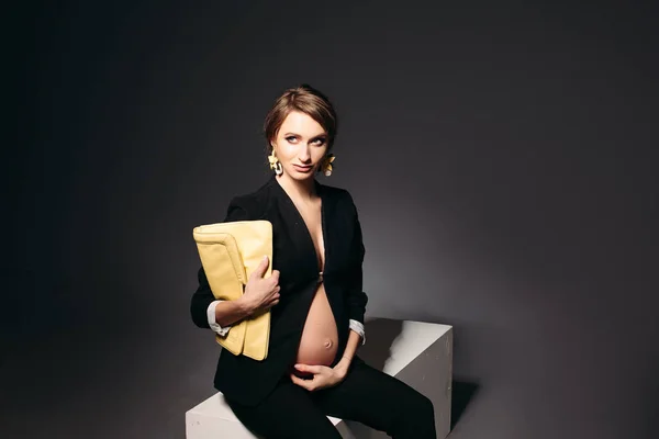 Femeie gravidă elegantă care stă pe fundalul studioului negru . — Fotografie, imagine de stoc