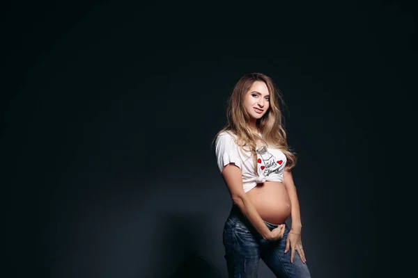 ジーンズのポケットで手を繋いでいるを着てスタイリッシュな妊娠中の女性. — ストック写真