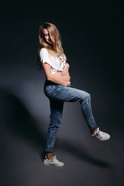 Mujer embarazada con estilo que lleva en jeans cogidos de la mano en los bolsillos . —  Fotos de Stock