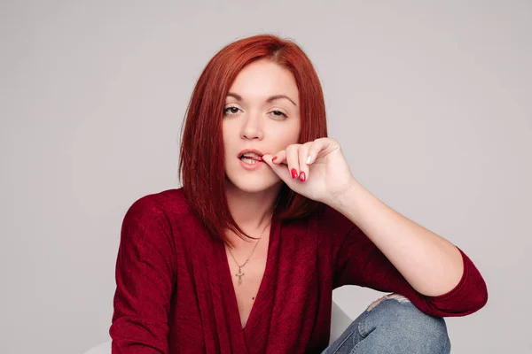 Model with ginger hair sitting on white chair in studio.